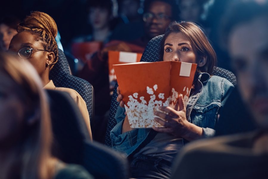 Scared woman watching horror film at movie theatre.